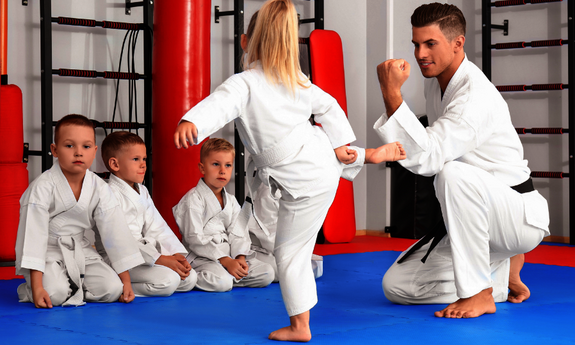 Ein Trainer übt eine Karateübung mit Kindern in der Sporthalle
