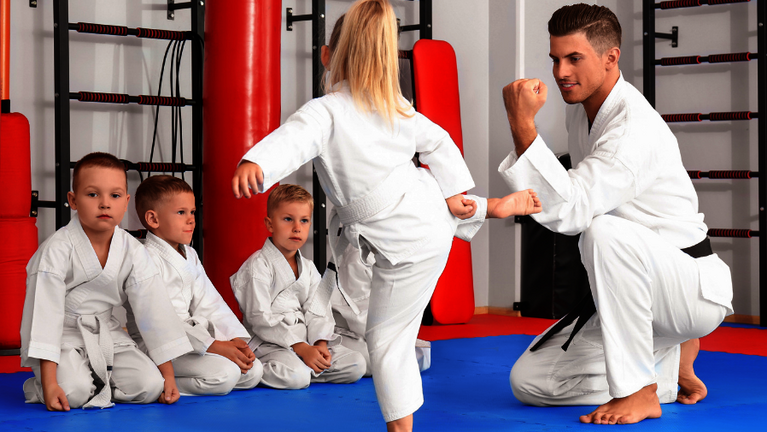 Ein Trainer übt eine Karateübung mit Kindern in der Sporthalle