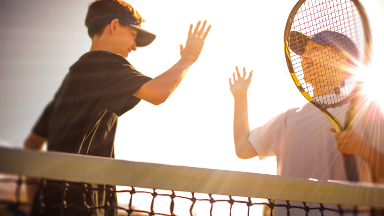 Zwei jugendliche Tennisspieler stehen am Netz und klatschen sich mit den Händen ab