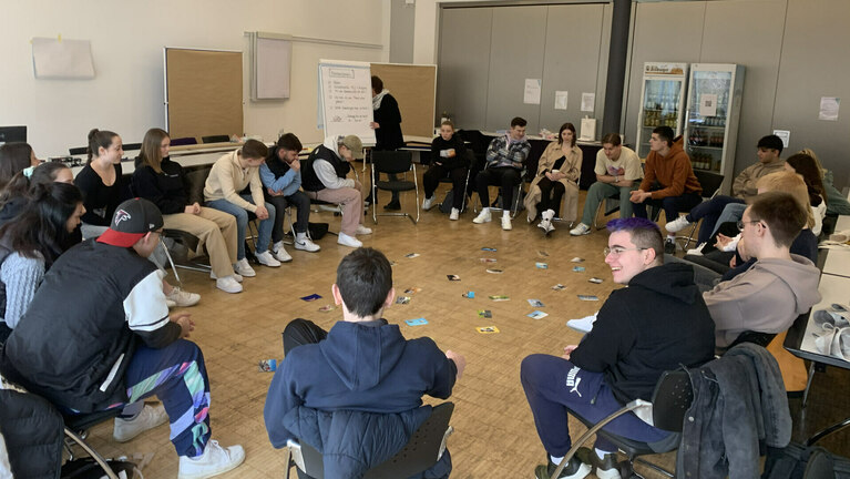 Teilnehmende einer Fortbildung sitzen im Kreis in einem Seminarraum