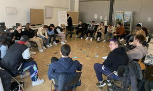 Teilnehmende einer Fortbildung sitzen im Kreis in einem Seminarraum