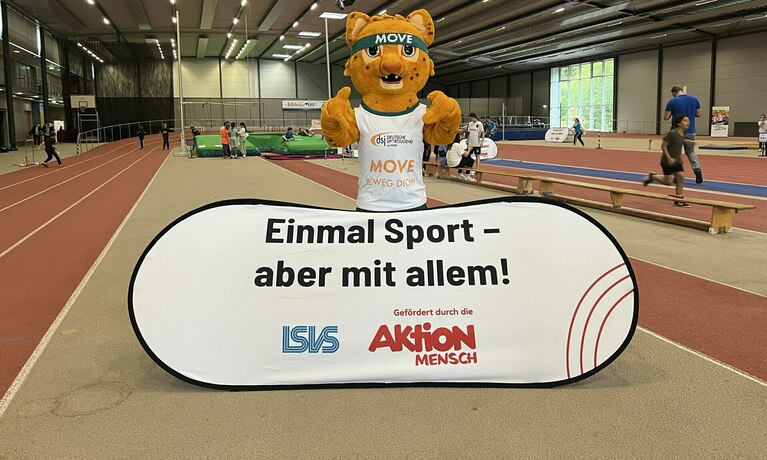 In  einer Sporthalle hält ein Bär einen Schild