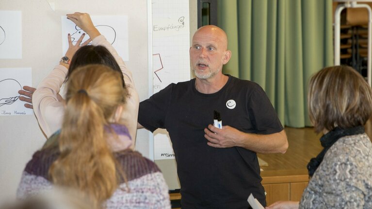 Ein erklärender Mann und zwei Frauen als Zuhörer