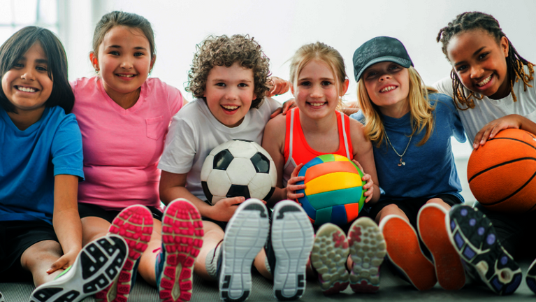 Kinder sitzen auf der Sporthalle auf dem Boden mit Bällen
