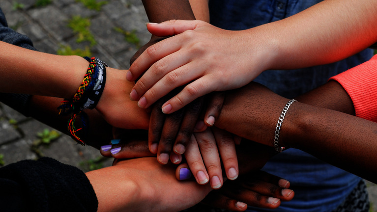 Sechs Hände sind über einander gelegt und halten zusammen