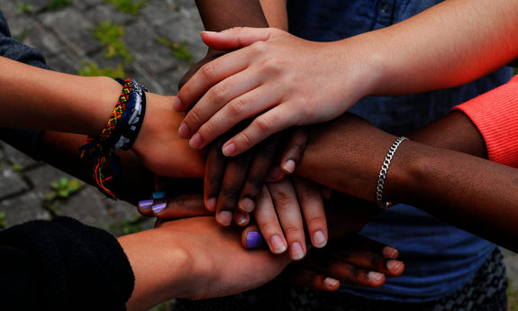Sechs Hände sind über einander gelegt und halten zusammen