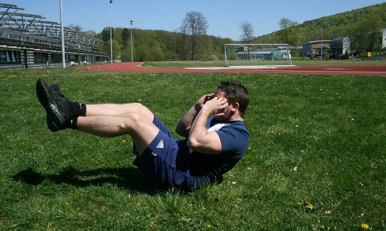 Sportler macht Fitnessübung auf Sportplatz.