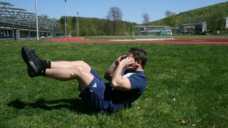 Sportler macht Fitnessübung auf Sportplatz.