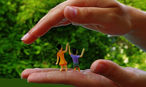 Zwei Hände vor dem Hintergrund der Natur legen sich schützend um zwei Kinderfiguren