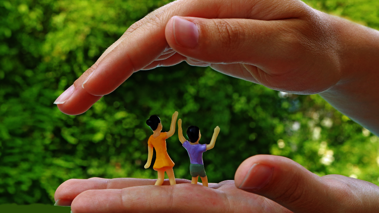 Zwei Hände vor dem Hintergrund der Natur legen sich schützend um zwei Kinderfiguren