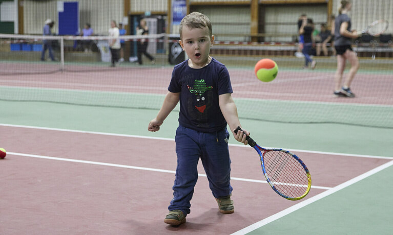 Ein kleiner Junge spielt in der Halle Tennis