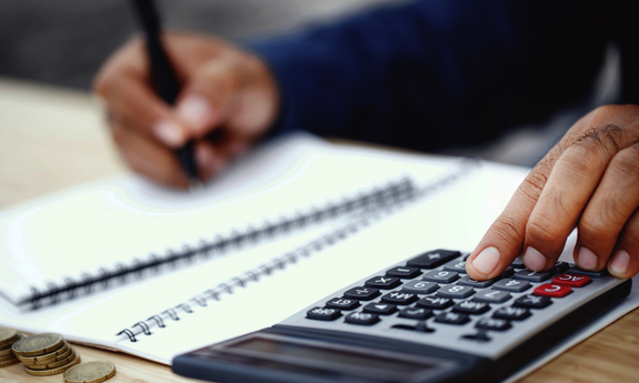 Bildausschnitt einer Hand beim Schreiben und Rechnen mit Taschenrechner