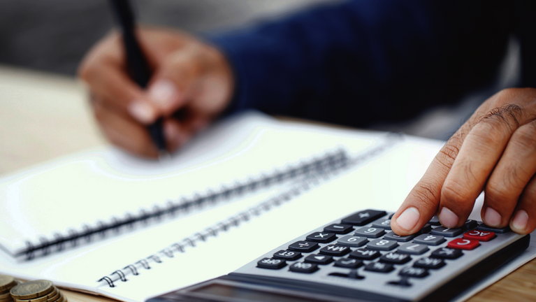 Bildausschnitt einer Hand beim Schreiben und Rechnen mit Taschenrechner