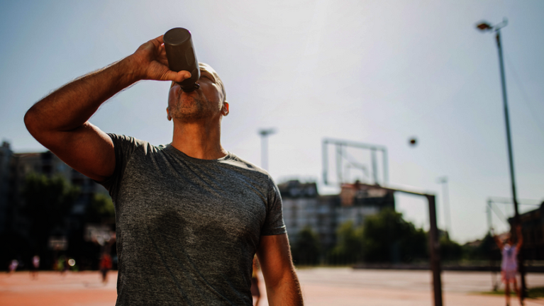 Ein Sportler auf dem Basektballplatz trinkt aus einer Trinkflasche