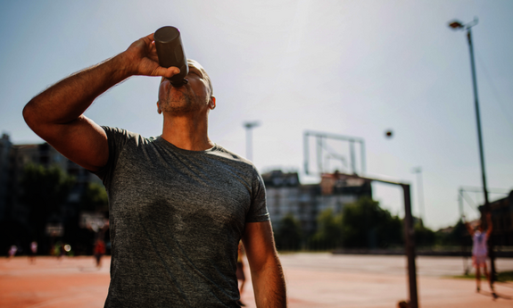 Ein Sportler auf dem Basektballplatz trinkt aus einer Trinkflasche