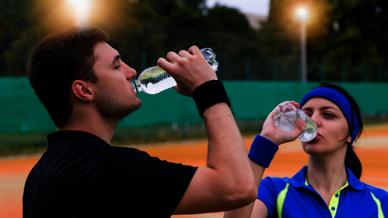 Ein Tennispieler und einen Tennisspiele trinken auf dem Tennisplatz in der Pause Wasser