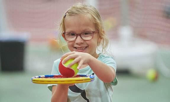 Ein Mädchen mit einem Softtennisball und einem Tennisschläger 