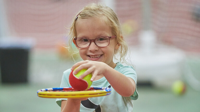 Ein Mädchen mit einem Softtennisball und einem Tennisschläger 