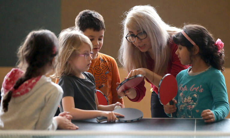 Übungsleiterin erklärt Kindern Tischtennis.