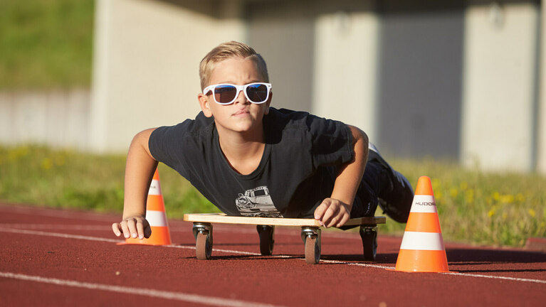 POA Ein Junge rollt auf einem Rollbrett über den Sportplatz