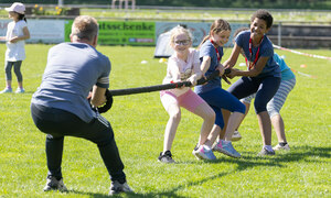 Ein Trainer und Kinder beim Tauziehen auf dem Sportplatz