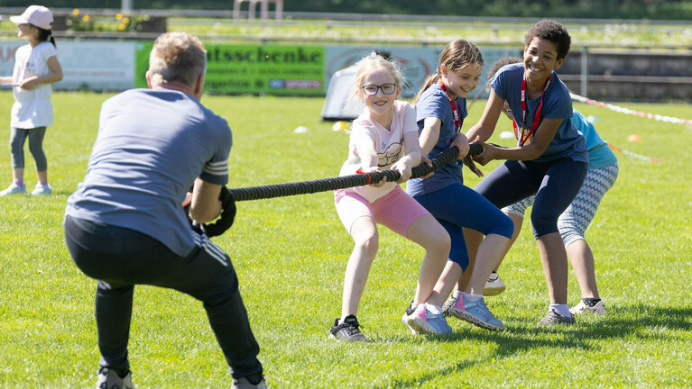 Ein Trainer und Kinder beim Tauziehen auf dem Sportplatz