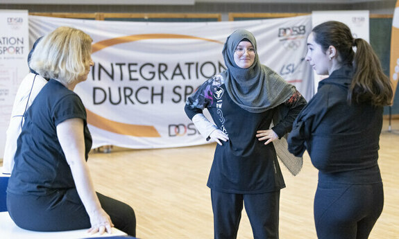 Vier Frauen aus verschiedenen Herkunftsländern stehen in der Sporthalle und tauschen sich aus
