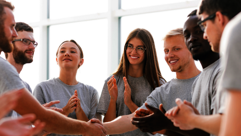 Eine Gruppe von jungen Menschen gibt sich im Kreis die Hand
