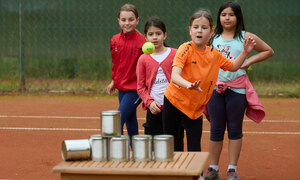 Vier Mädchen spielen auf dem Sportplatz ein Wurfspiel mit Dosen
